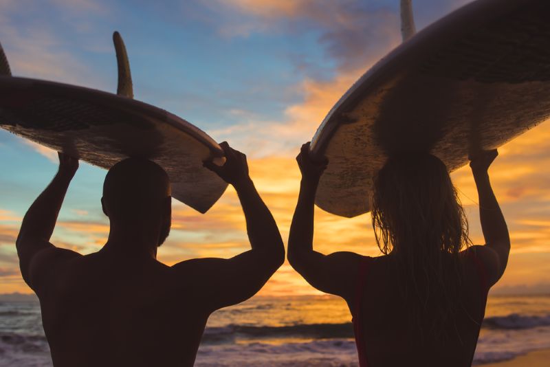 Two men holding surfboards over their head at sunset